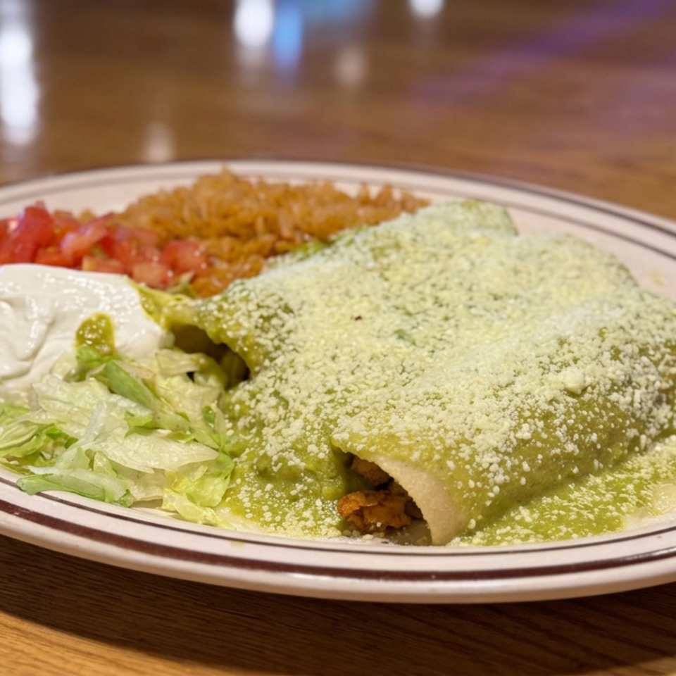 Mexican plate featuring green-sauce enchiladas topped with cheese, alongside lettuce, sour cream, pico de gallo, and rice.